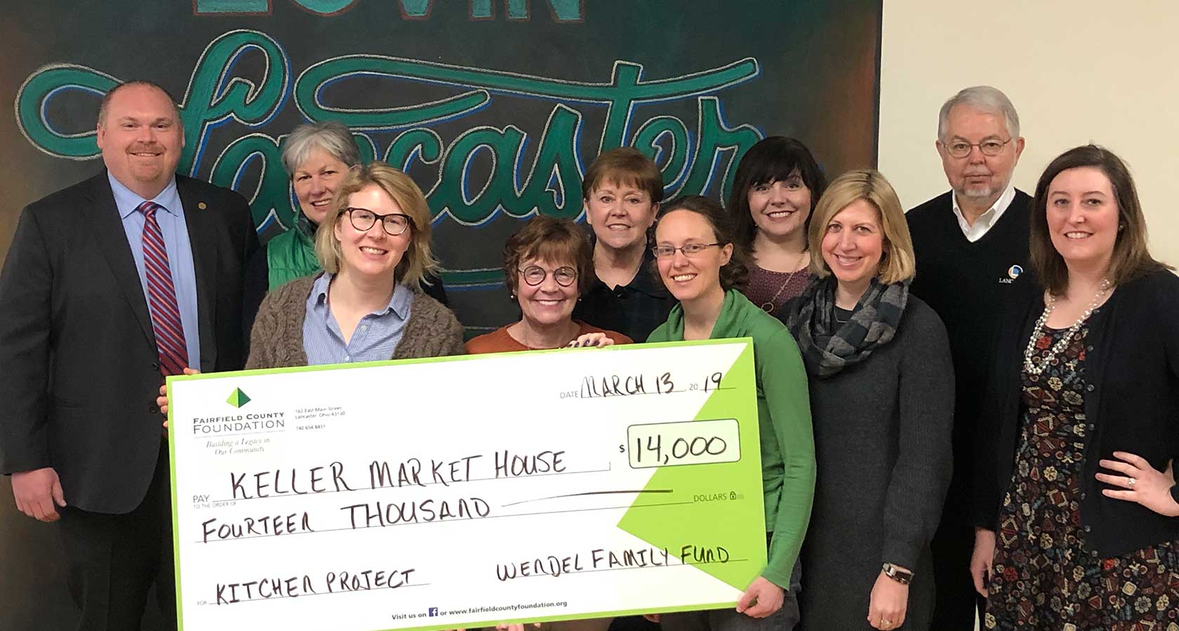 Group of people holding large display check for $14,000 with ‘Kitchen Project’ in note area signed by the Wendel Family Fund.