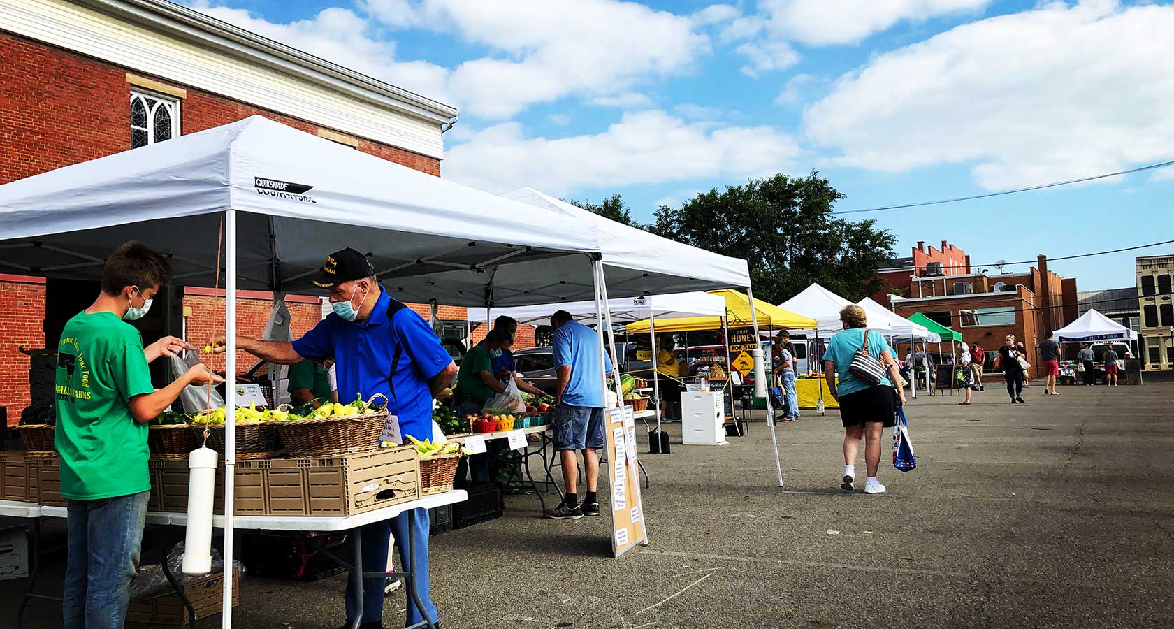 Scene of vendors and shoppers at farmer’s market tents