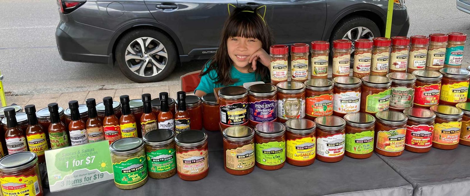 Young girl smiling behind display of Montezuma brand sauces and salsas