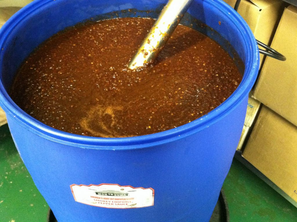 Large blue container of smokey chipotle pepper sauce in production at Chuck Evans’ Montezuma sauces