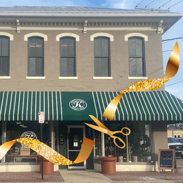 gold ribbon and gold scissors stretched across a tan market house building with green & white striped awning