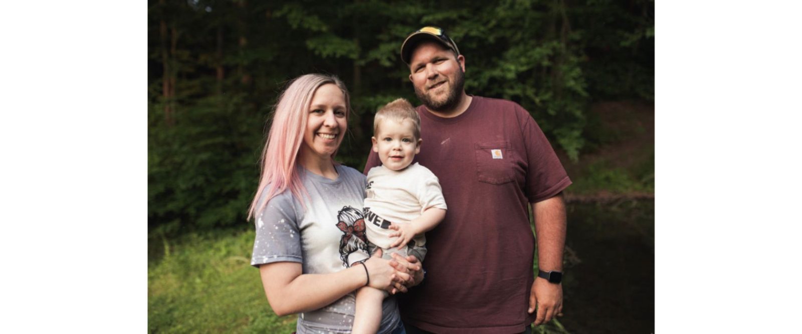 a posed family photo, a man in a maroon tshirt, and a woman with long hair dyed pink holding a young boy