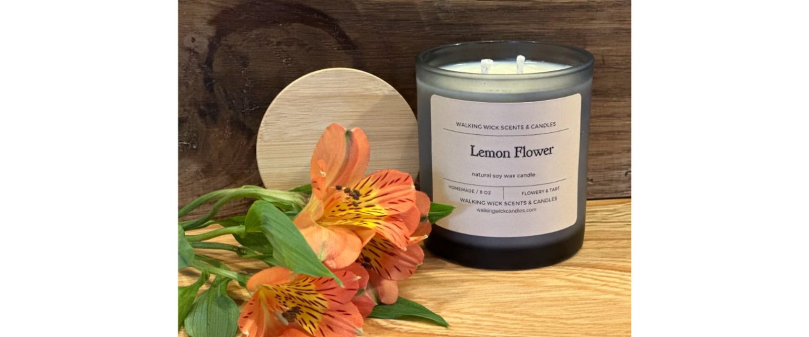 a "lemon flower" scented poured soy wax candle in a jar displayed with a wooden lid and an orange tropical flower