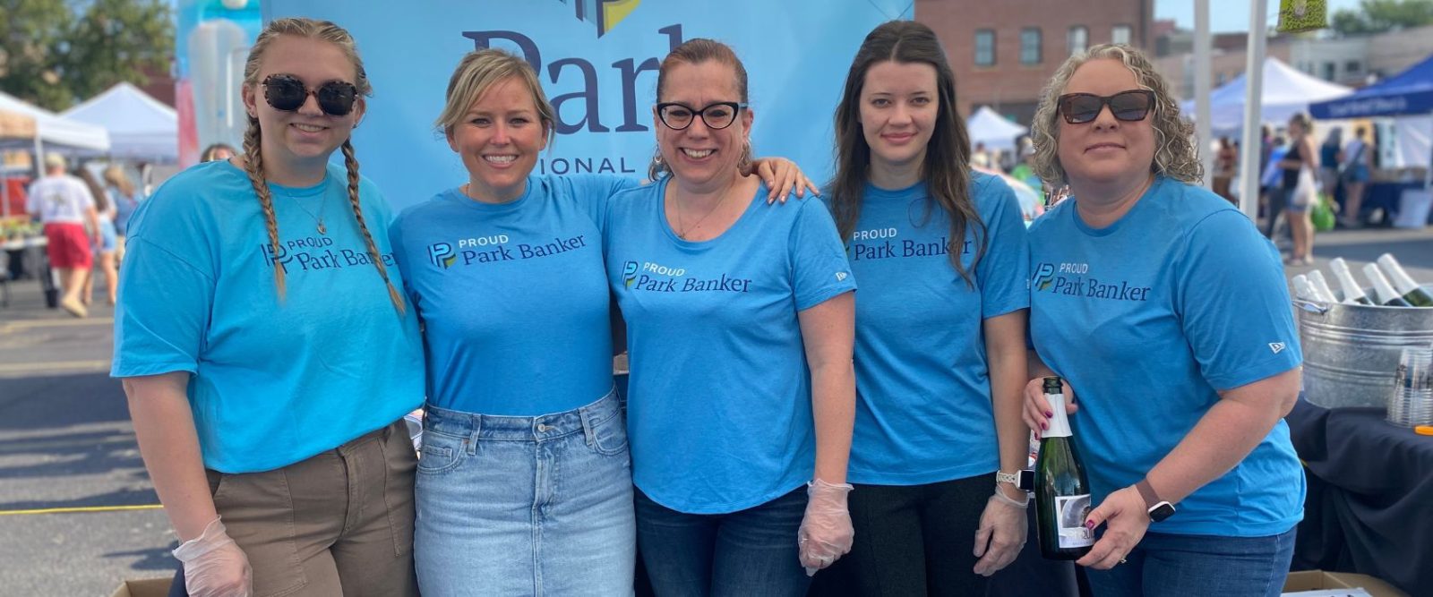 group of women in bright blue Park National Bank tshirts, posing outside for the camera in front of bank banner