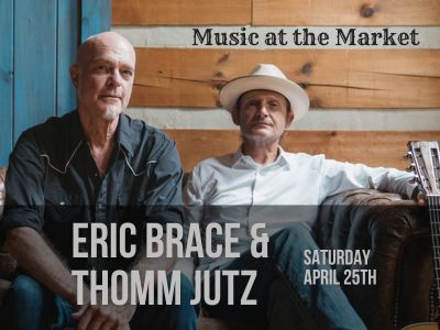 two men seated on a couch and looking at the camera, one in a cowboy hat